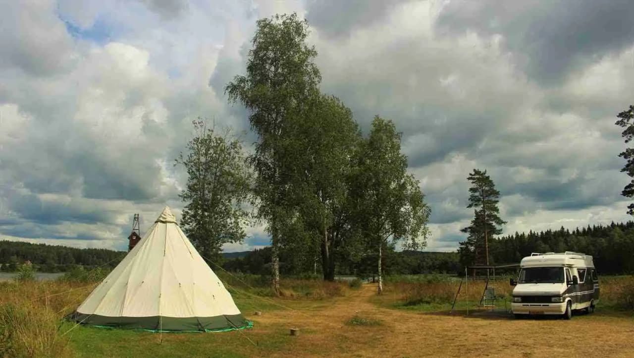En tältplats på Sörälgens camping, omgiven av gräs och öppna ängar, med ett tält uppsatt på en grön gräsyta under en klar himmel.