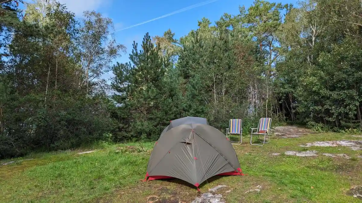En solig dag vid Almöns bad & camping med tält uppsatta bland grönskande skog, omgiven av frodig växtlighet och natur. Perfekt för friluftsliv och avkoppling.