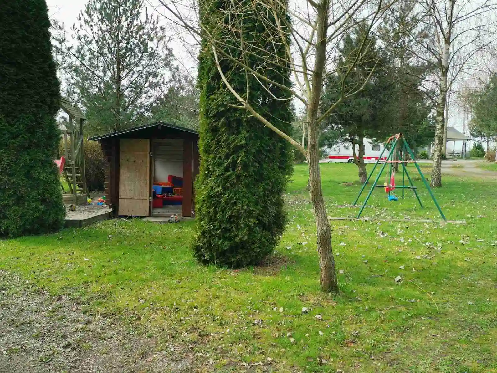 Bild av Fredriksbergs kursgård-camping: En frodig trädgård med buskar, gräsmatta och koniformade barrträd. Häggen avgränsar gräsmattan i bakgården, vilket skapar en inbjudande och välskött landskapsmiljö.