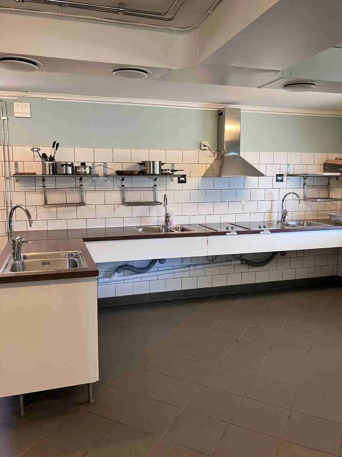 Interiörbild av ett kök med modernt inredd design. Köksgolvet är av trä och det finns en diskho, köksbänk och köksmaskiner. Taken är vitmålade och ger ett ljust och luftigt intryck.