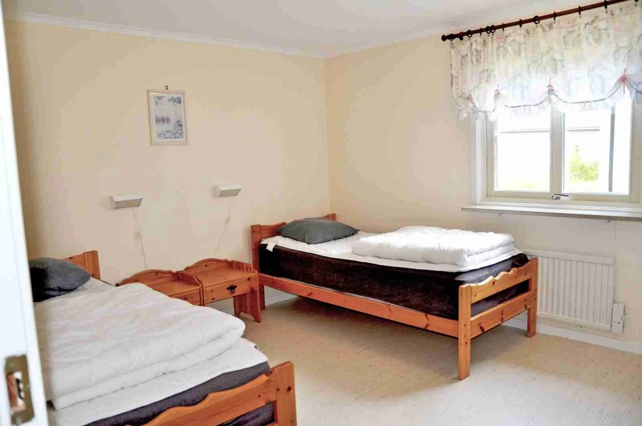 En ljus och inbjudande sovrumsmiljö med en stor säng klädd i vita sängkläder, omgiven av trädetaljer och en träfärgad golvyta.