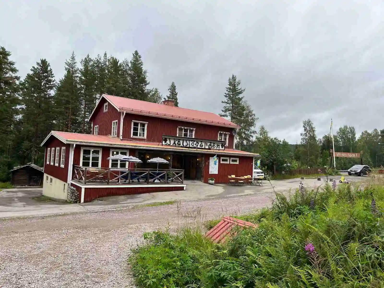 En träbyggnad med en veranda omgärdad av barrträd, som erbjuder en avkopplingsplats vid Skålsjögården Timber Lodge.