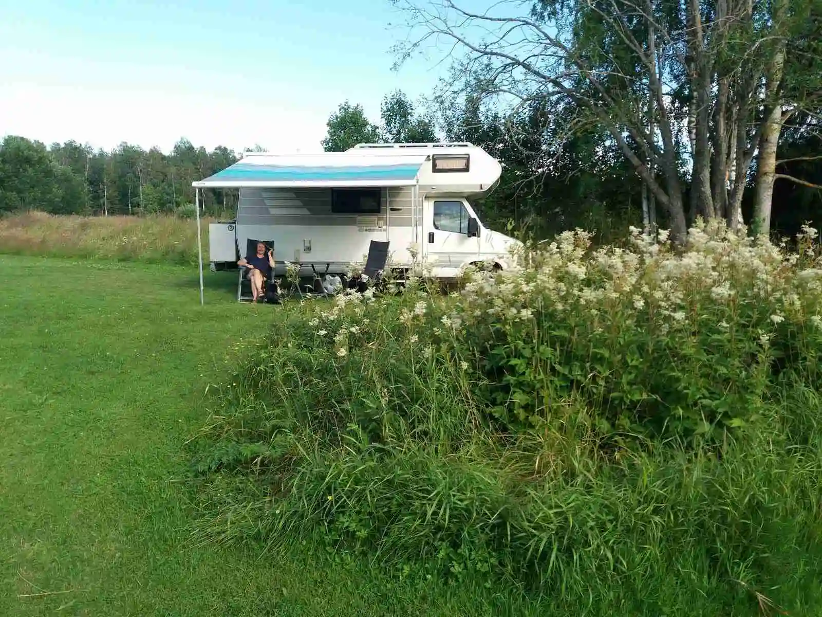 En grön äng med husvagn och prärieväxter vid Vreten Kursgård i bakgrunden.