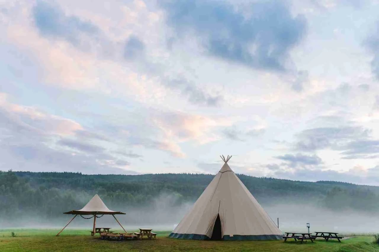 En campingplats med tält uppställda i en naturpark, omgiven av öppet landskap och grönska.