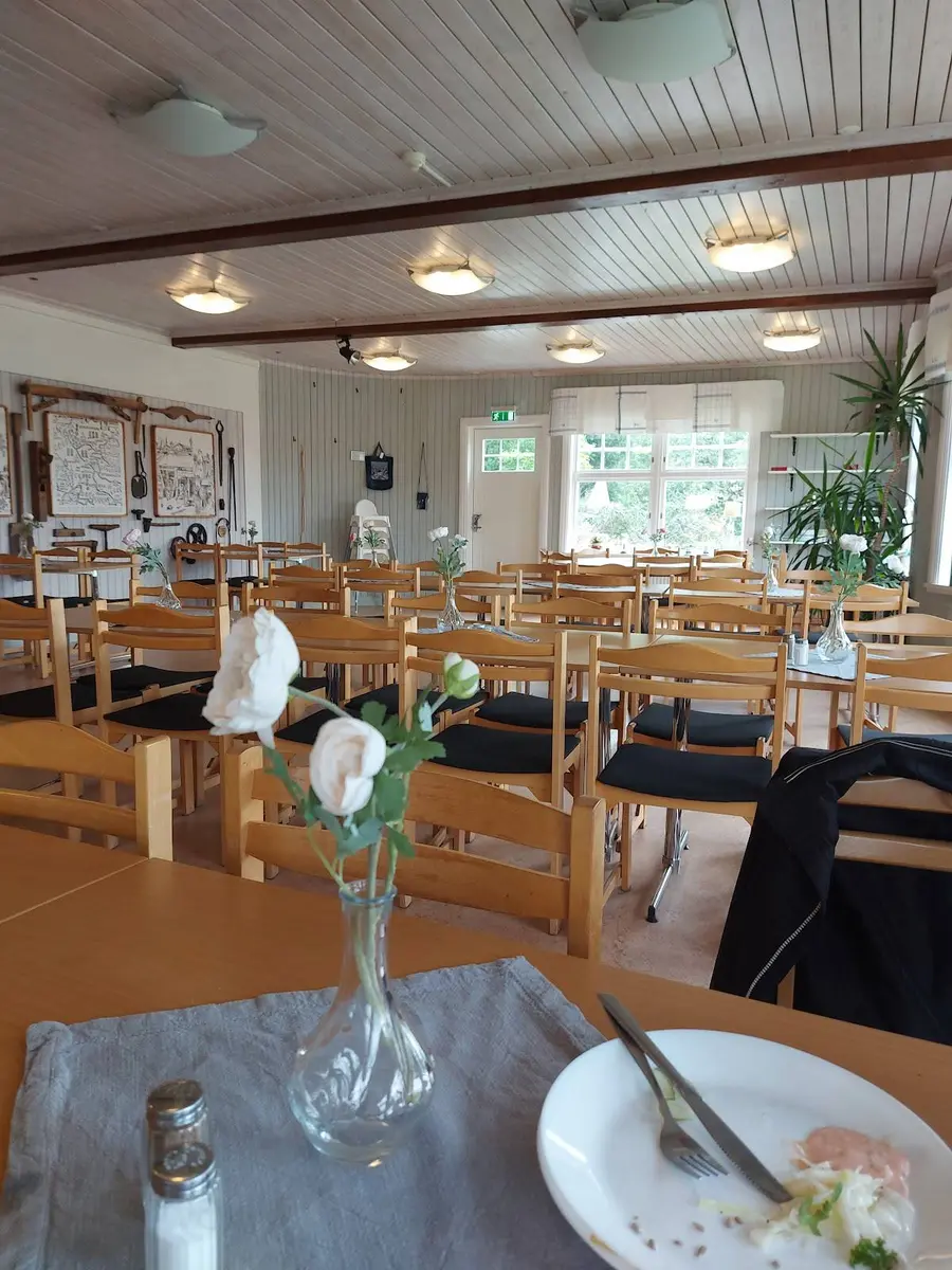 Ett ljust och rymligt matrum på Uskavigårdens camping, inrett med flera bord och stolar. Golvet är av trä och det finns stora fönster som släpper in dagsljus, vilket ger en inbjudande och trivsam atmosfär för besökare.