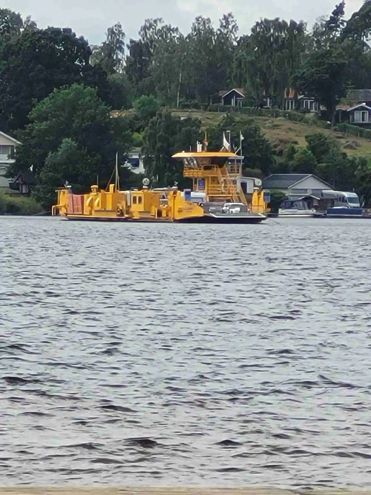 En segelbåt ligger stilla på en rofylld sjö vid Ivö Camping, omgiven av en naturskön vy med träd i bakgrunden.