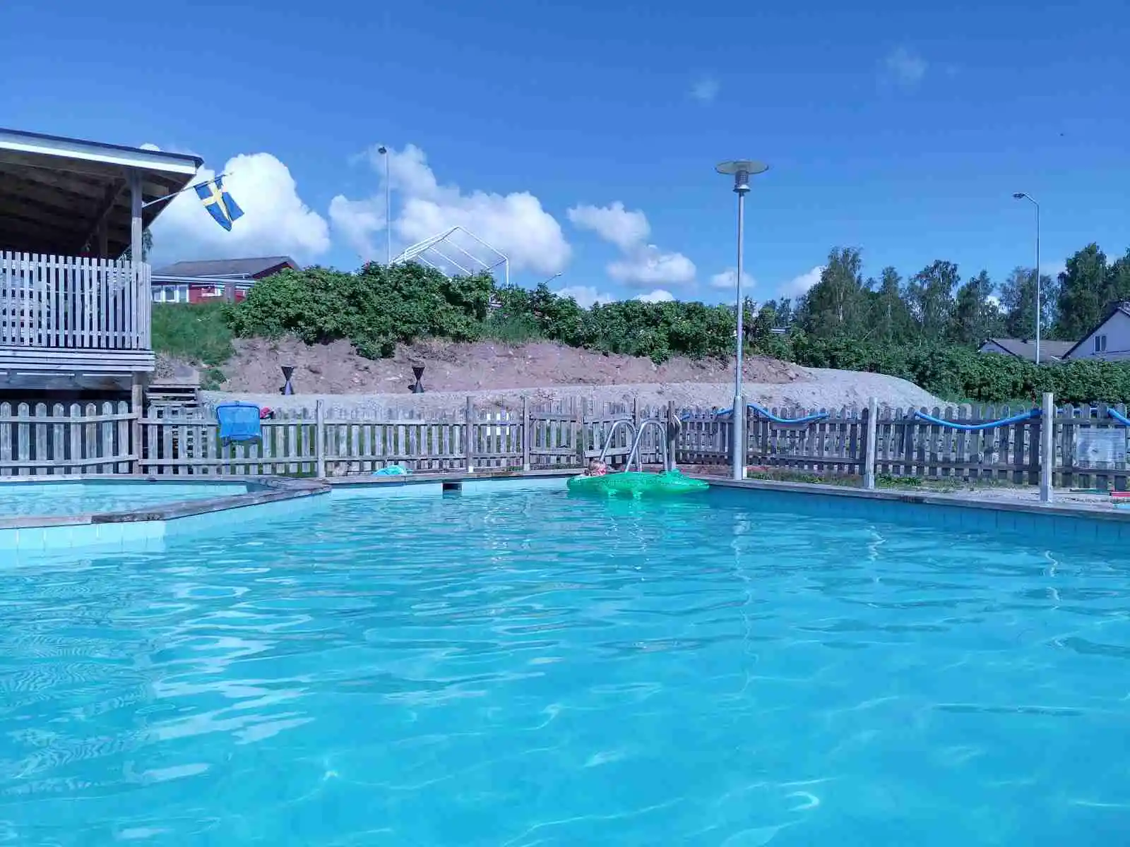 En utomhuspool på Vegby Camping omgivet av solstolar och ett stängsel, vilket skapar en avkopplande semesterstämning.