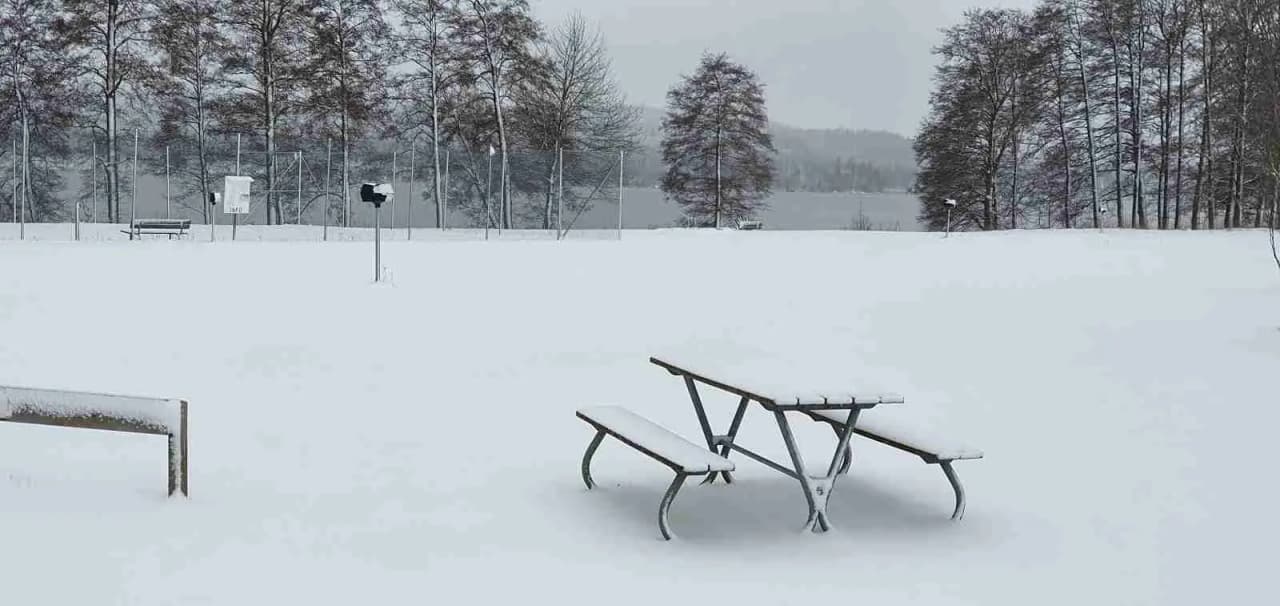 En snöig vinterdag vid Ramkvilla camping, med snötäckta grenar och en frusen utomhusbänk.