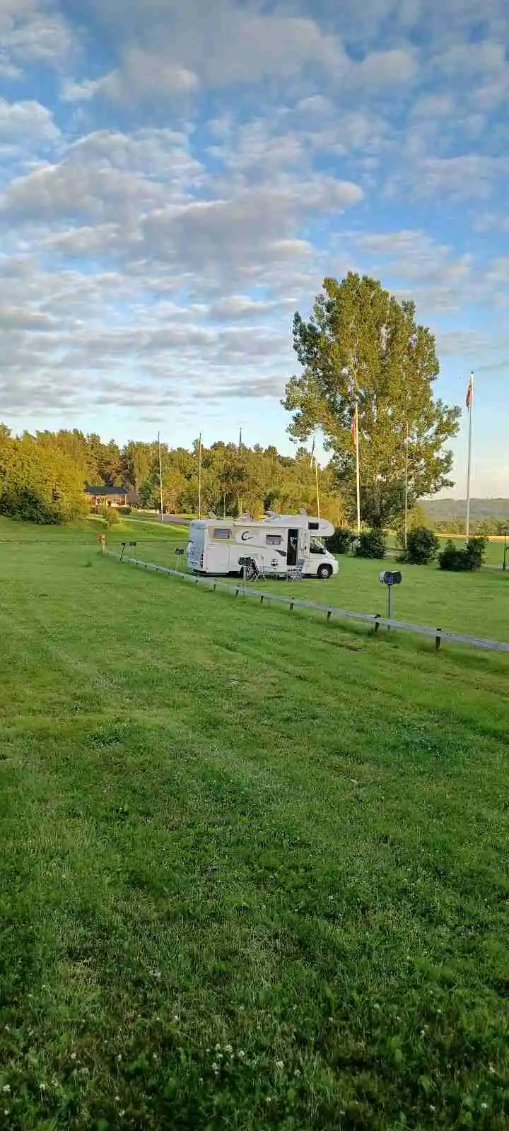 En grön campingplats med husbilar och husvagnar parkerade på ett stort gräsfält i Tanums camping och stugby.