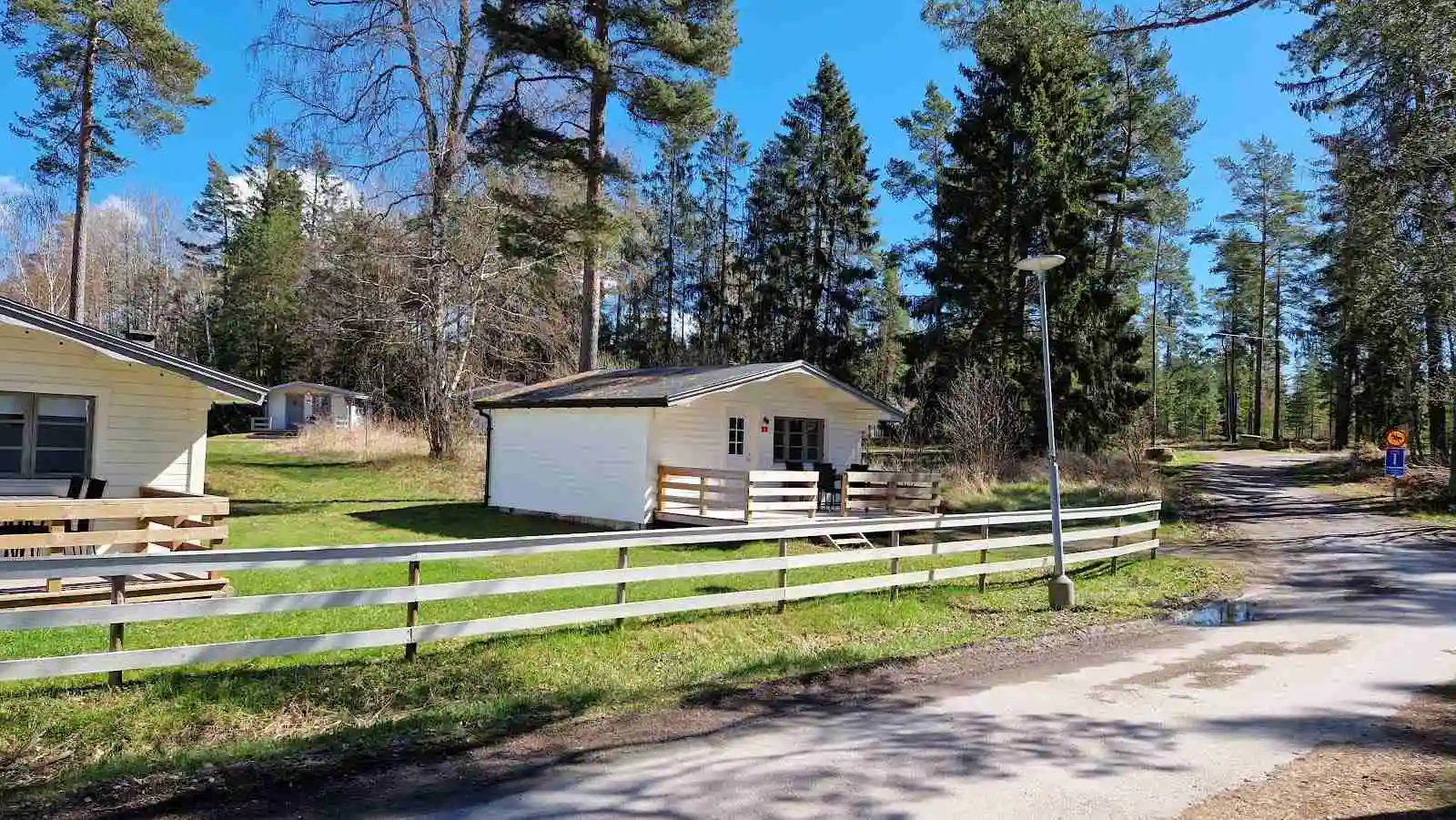 Bild av Malexander Camping visar en grönskande landskap med träd, gräs och växter. I bakgrunden syns en stuga som smälter in i den natursköna lantliga miljön.