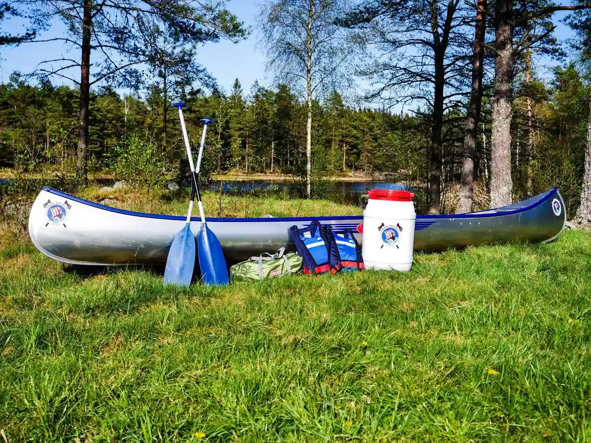 En kanot ligger vid en stilla sjö, omgiven av grönskande skog, redo för paddling och äventyr i naturen.