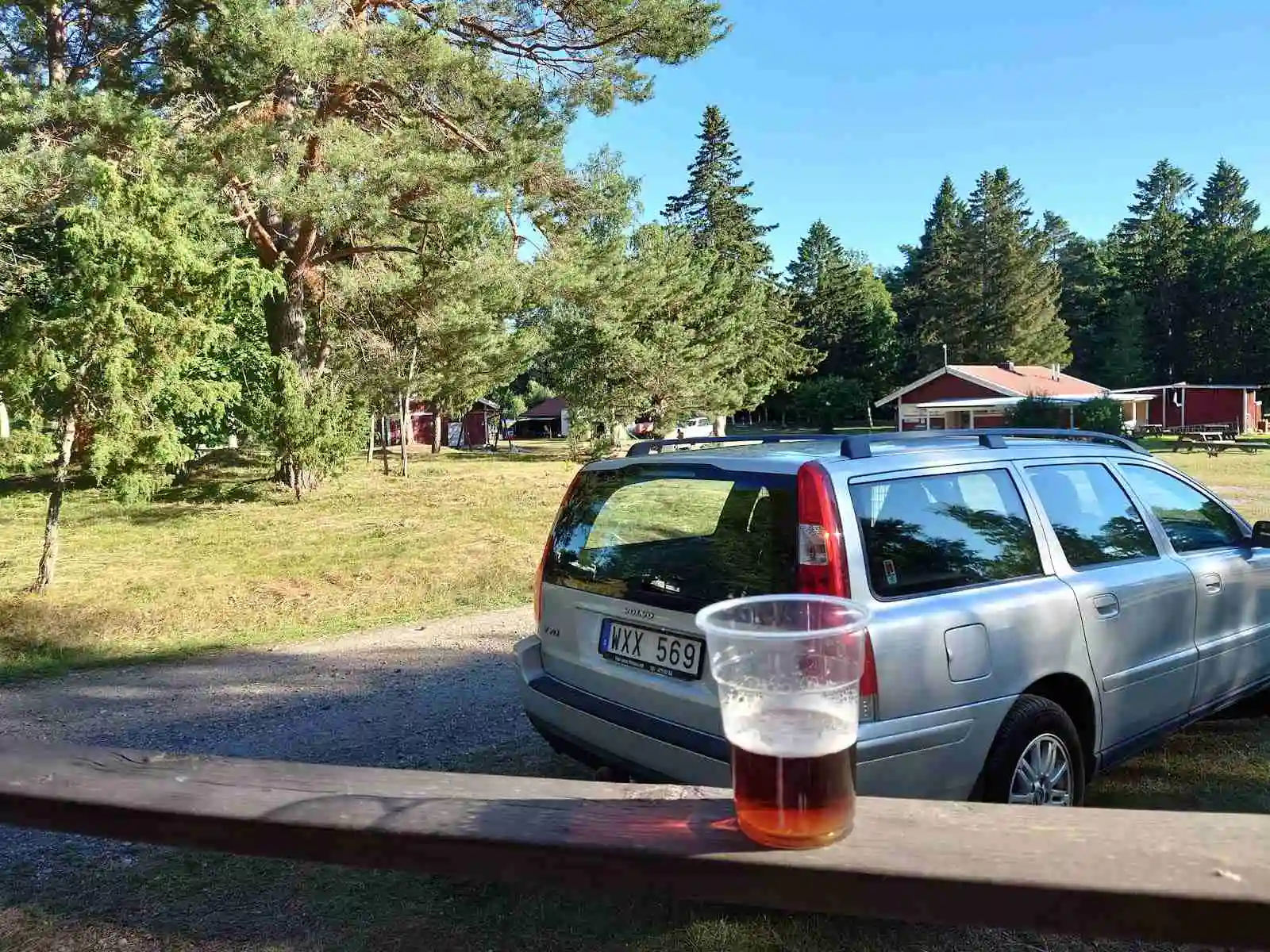 En familjebil, med öppet bagageutrymme, parkerad på Kapellskärs camping. Baklyktor och typiska Volvo-detaljer syns tydligt. Det är en SUV som står på en grusväg, omgiven av natur.