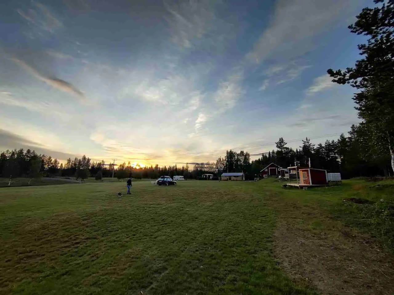 En somrig landskapsbild av Orrkulla Camping med klar himmel, grönt gräs och mjuka moln i bakgrunden, perfekt för en avkopplande vistelse nära naturen.