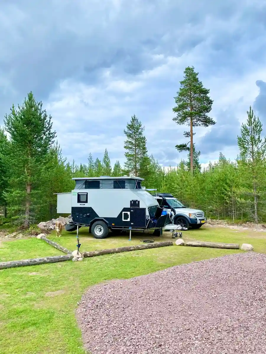 En stor rekreationsfordon står parkerad på en lerig offroadcamp-plats, omgiven av robusta däck och tydliga spår i marken, redo för äventyr.