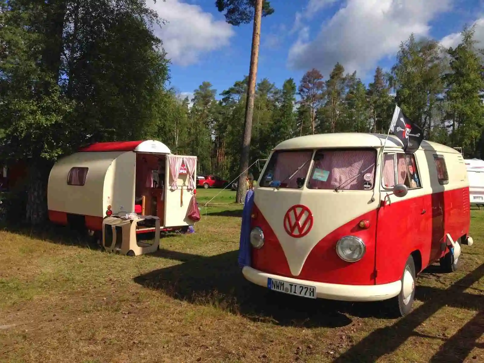 En Volkswagen husbil parkerad på en camping med ett tält uppsatt bredvid, omgiven av grönska på Norraryds camping.