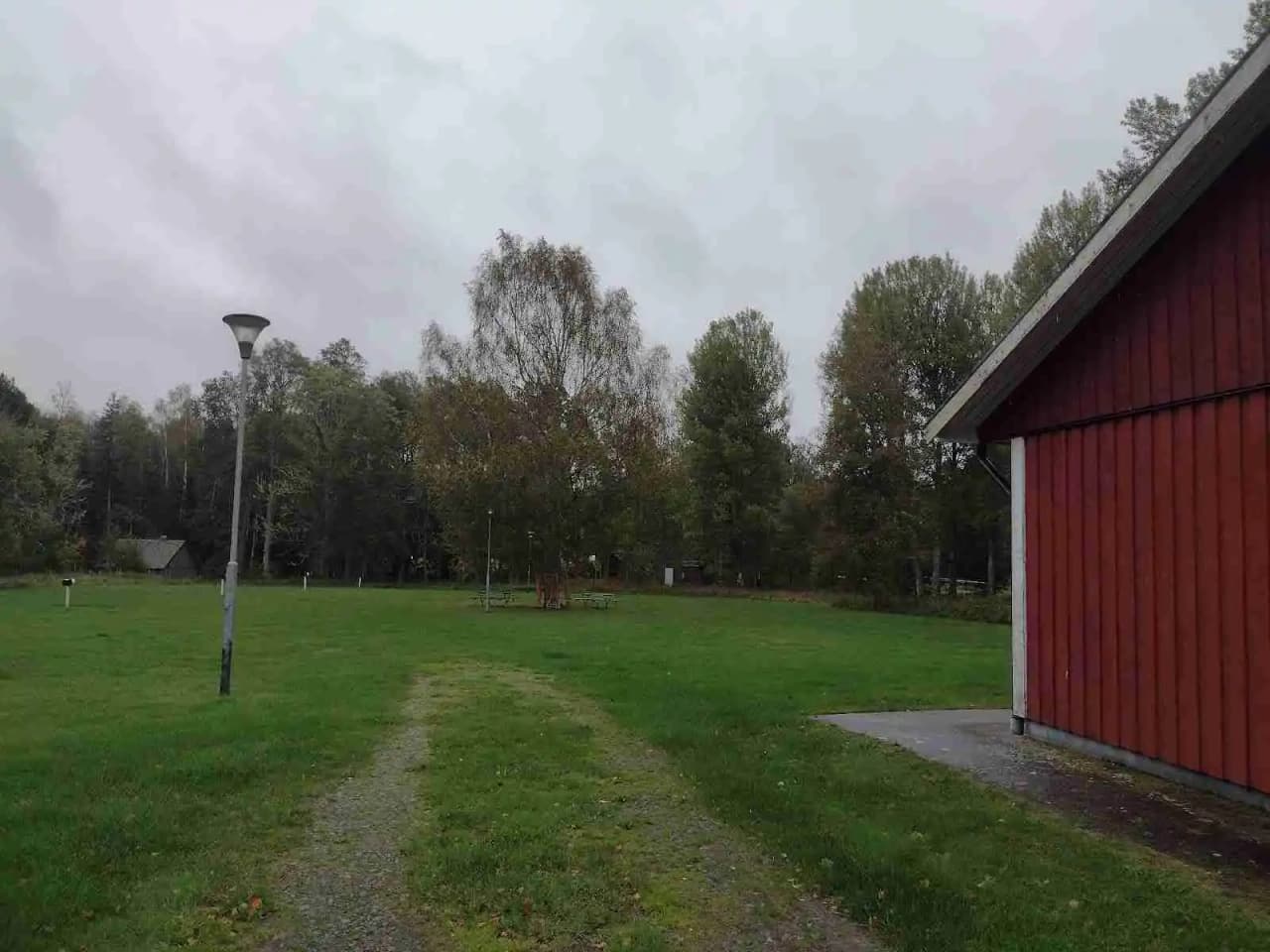 Alt-text: En vidsträckt gräsmark omgiven av träd och buskage vid Emmaboda Camping, med ett stort grönt fält som skapar en lugn och naturskön miljö.