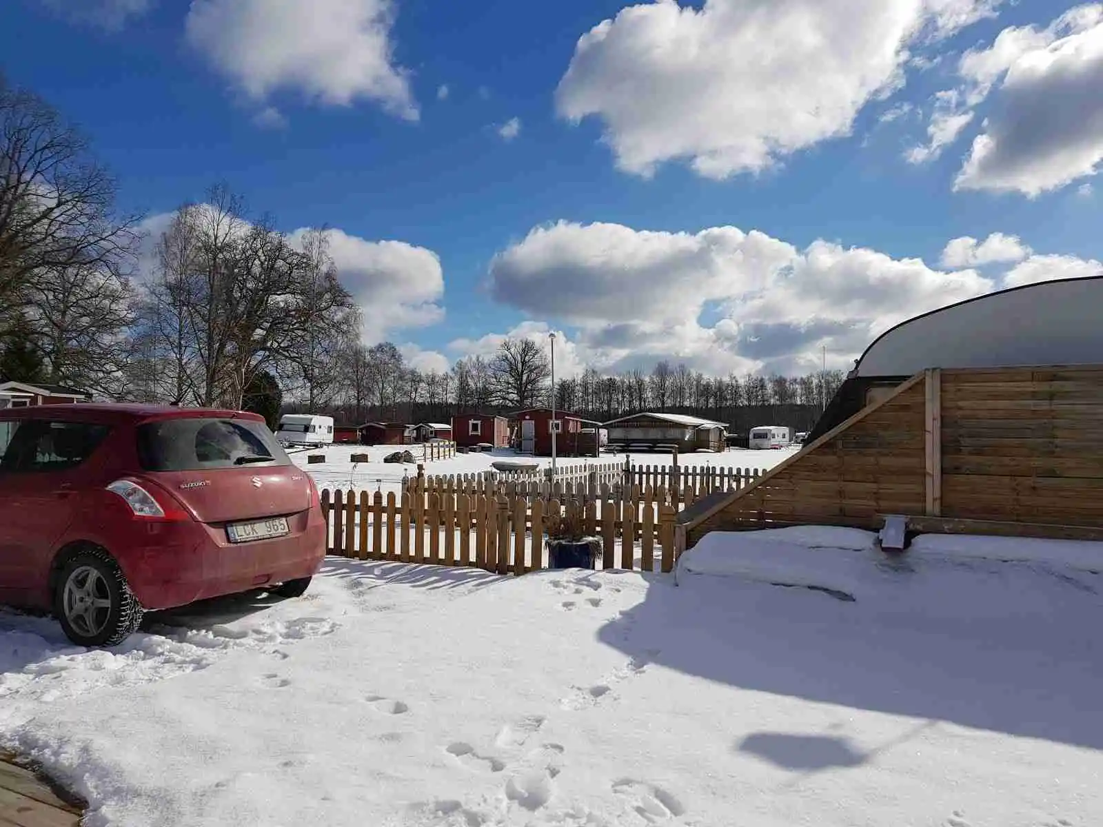 En snötäckt campingplats vid Österby camping, med flera bilar parkerade i vinterlandskapet. Bilarna har synliga baklyktor och är täckta av snö, vilket skapar en typisk vintermiljö.