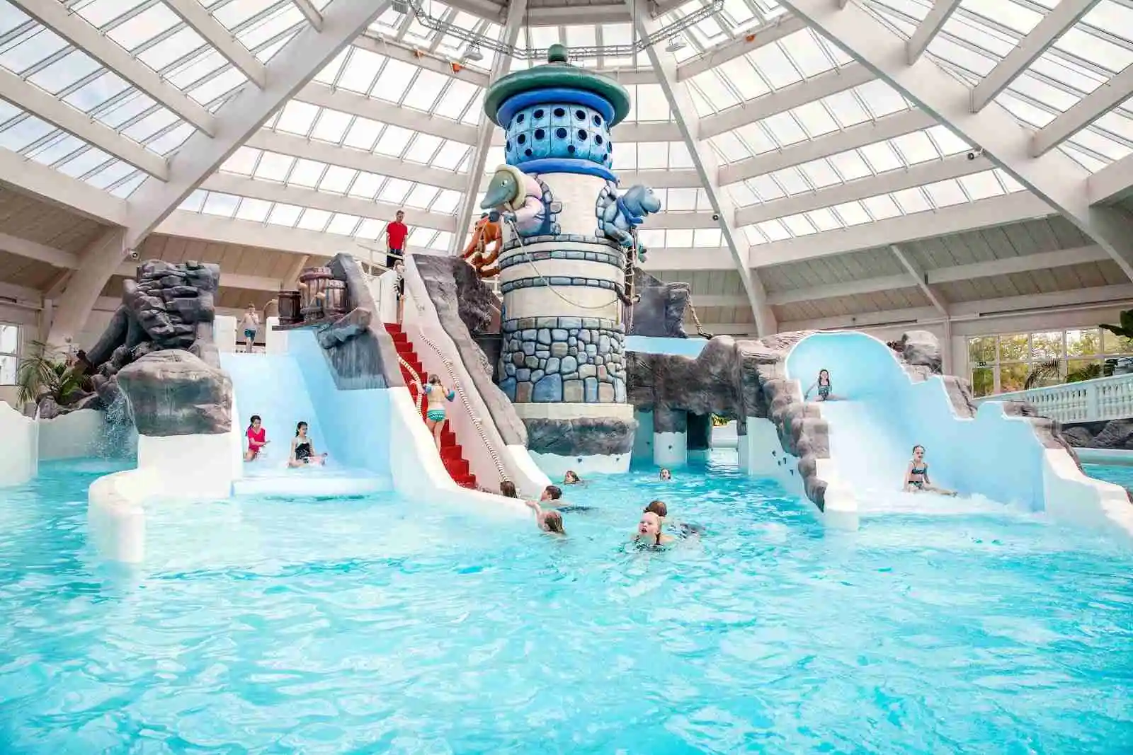 En livfull bild av Västervik Resort som visar en stor pool omgiven av glada semesterfirare. På området syns även vattenrutschbanor och andra lekattraktioner, vilket förstärker platsens inbjudande och avslappnade atmosfär. Perfekt för en rolig och avkopplande familjesemester.