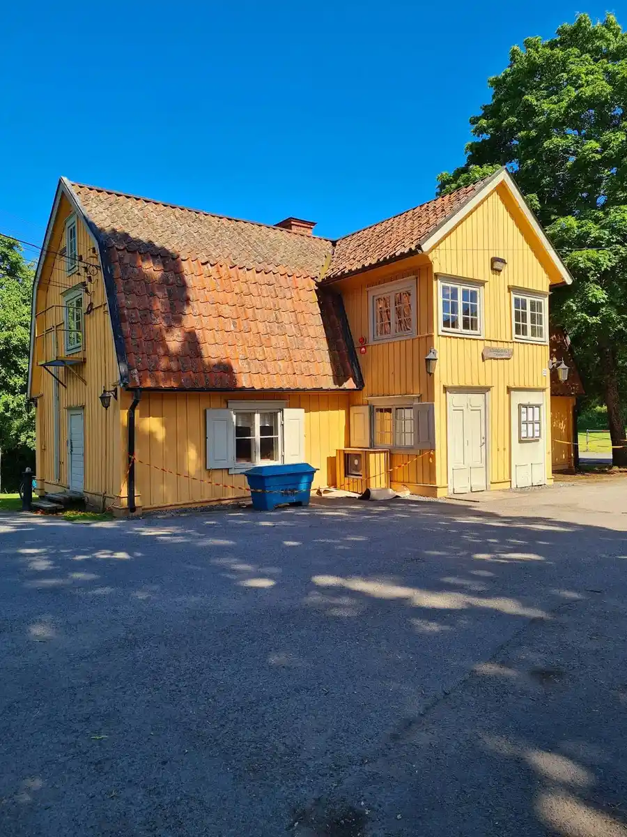 Bild av Klubbensborg: ett mysigt stugliknande hus med sadeltak och flera fönster med spröjs. Det finns en synlig dörr och en uppfart som leder fram till byggnaden, vars fasad är täckt med panel.