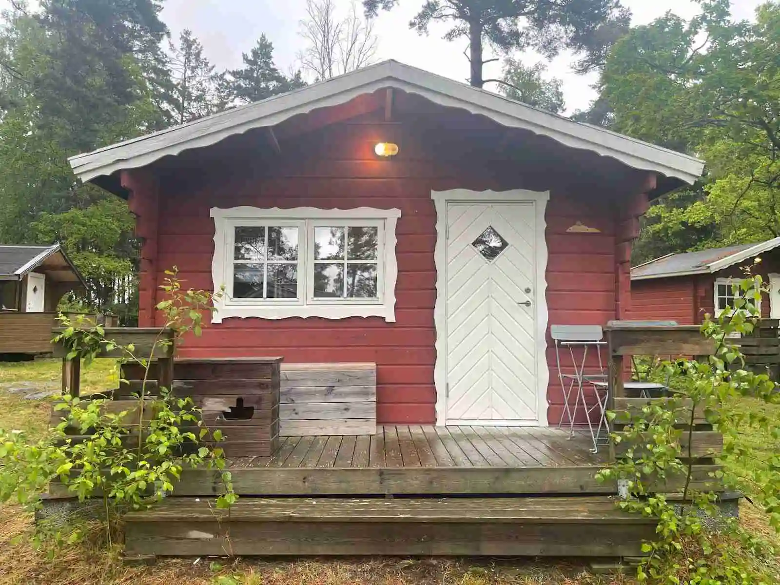 En liten trästuga vid Waxholms camping, omgiven av grönska med en liten veranda och en trädörr.