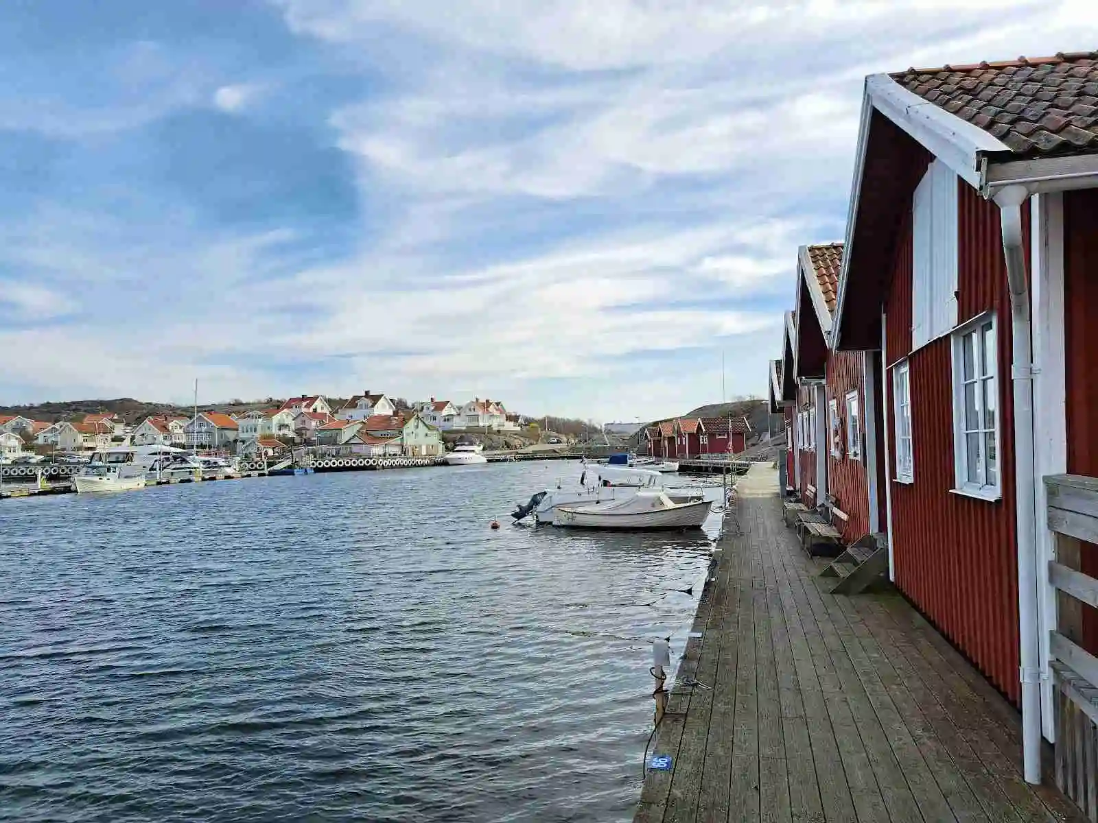 En vy över Hunnebostrands camping och stugor, som visar en livlig marina med motorbåtar ankrade vid bryggan och en naturskön vattenväg omgiven av grönska.