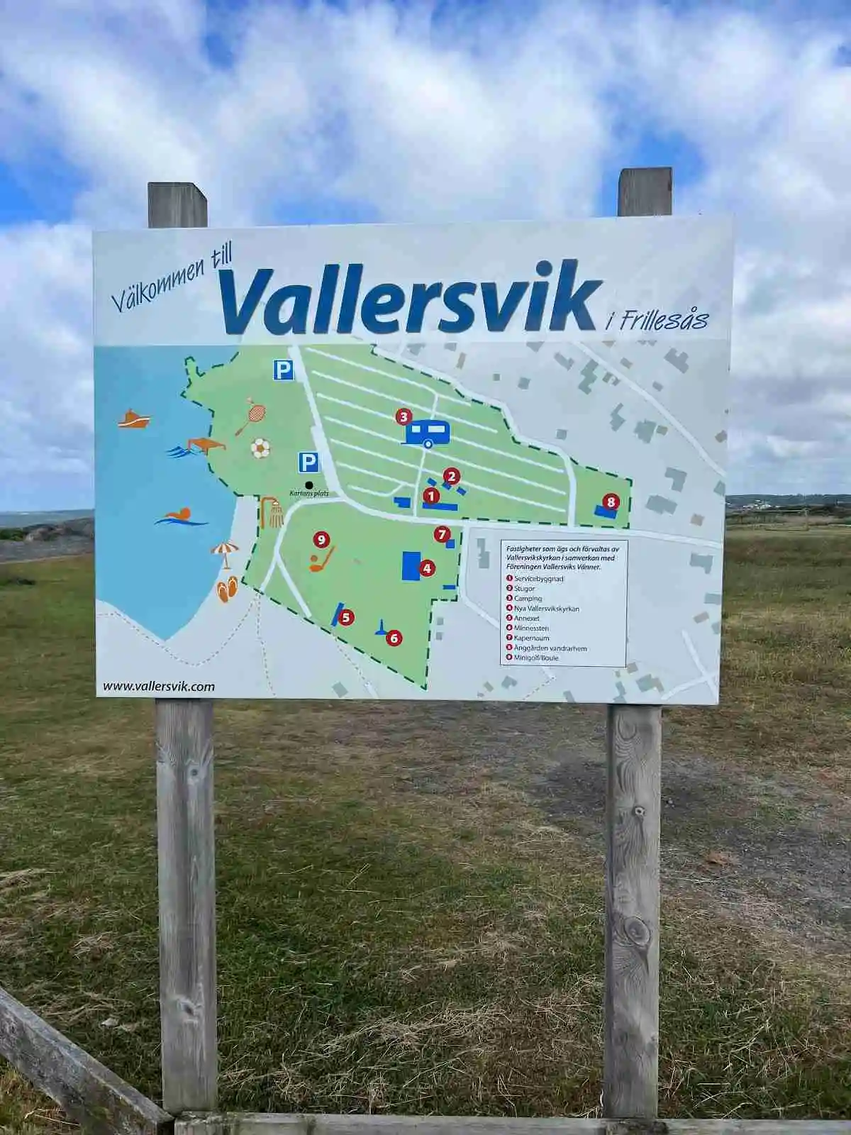 En grönskande äng med en grusstig leder fram till en skylt vid Vallersvik Camping och Vandrarhem.