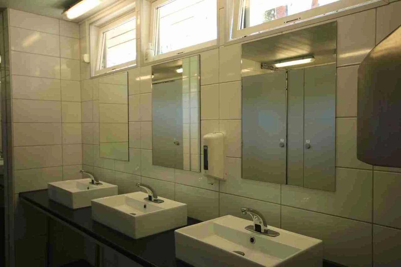 Bild på ett badrum i Rösjöbaden Camping & Stugby. Visar ett handfat med en modern kran, ljusa väggar och golv, samt ett stilrent och rent intryck i interiördesignen.