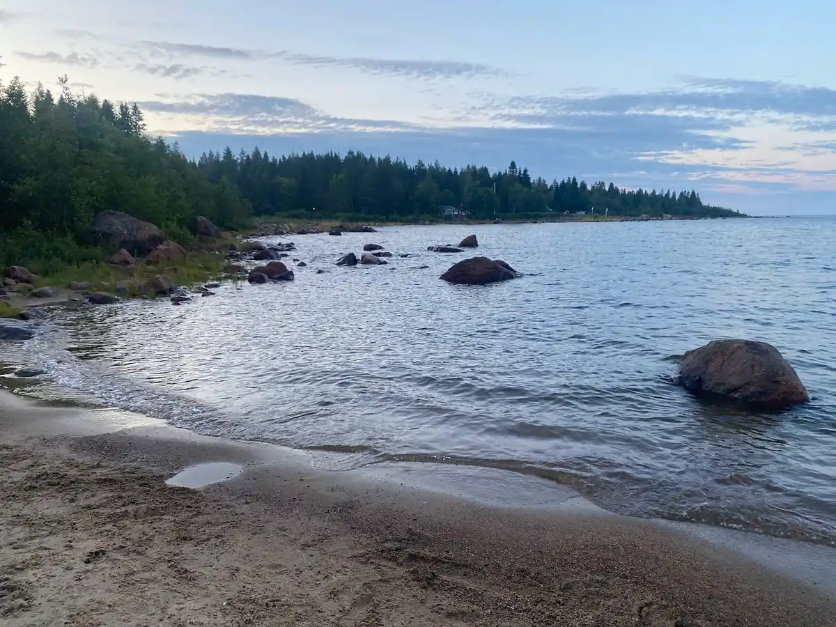 En vacker kustlinje med en sandstrand och stora klippblock, omgiven av det blå havet under en klar himmel. Perfekt för camping och avkoppling vid havet.