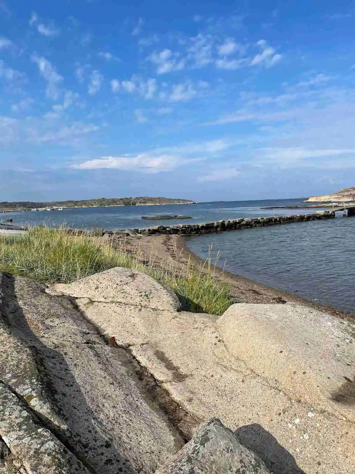 En naturskön strandlinje vid Kyrkvikens Camping med glittrande vatten och omgivande klippor i bakgrunden.