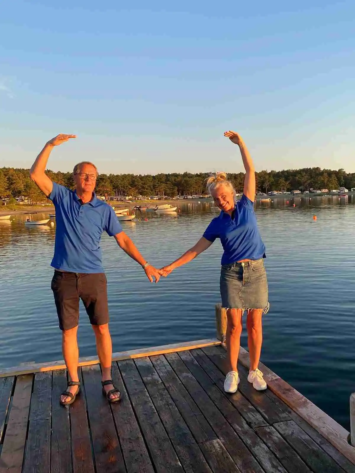 En grupp människor njuter av en solig dag vid sjön på Kyrkviken Camping. Några går i shorts och deltar i fritidsaktiviteter vid vattnet.