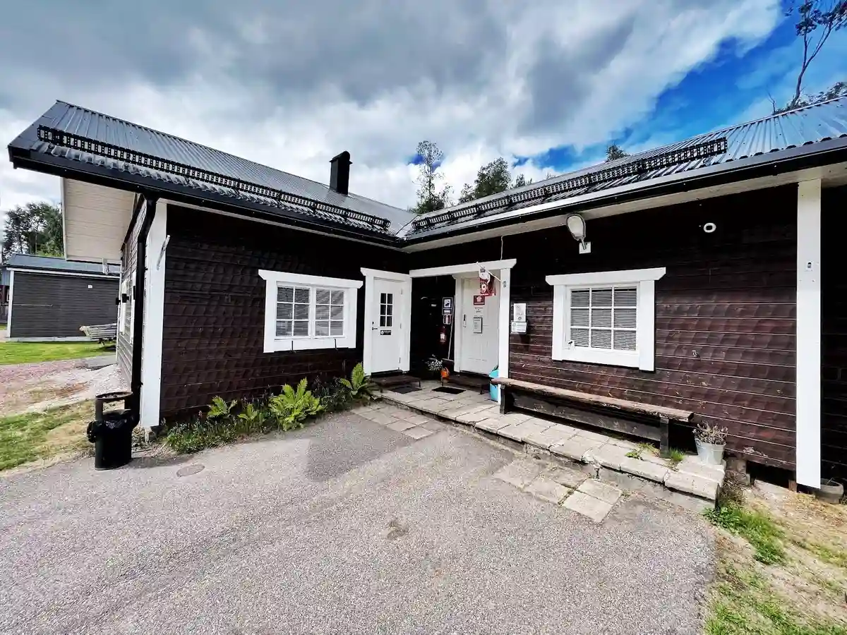 En idyllisk stuga med rött tak och träfasad, omgiven av grönska och en rymlig gårdsplan på Lillhärdals camping.