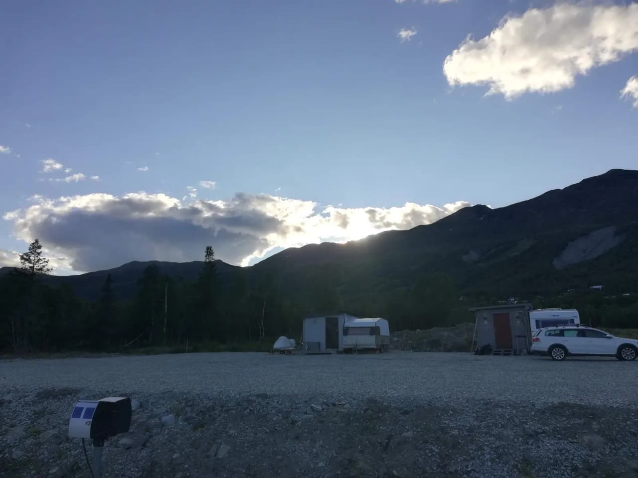 En lastbil kör på en väg omgiven av höga berg och böljande kullar under en himmel med molnformationer i Kittelfjäll.