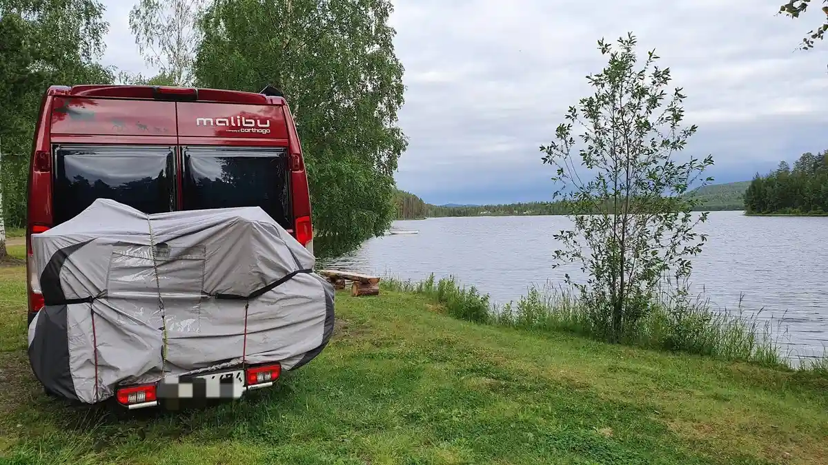 En husbil parkerad på en campingplats med en utsikt över Lapplands vildmark, omgiven av tält och andra campingfordon.