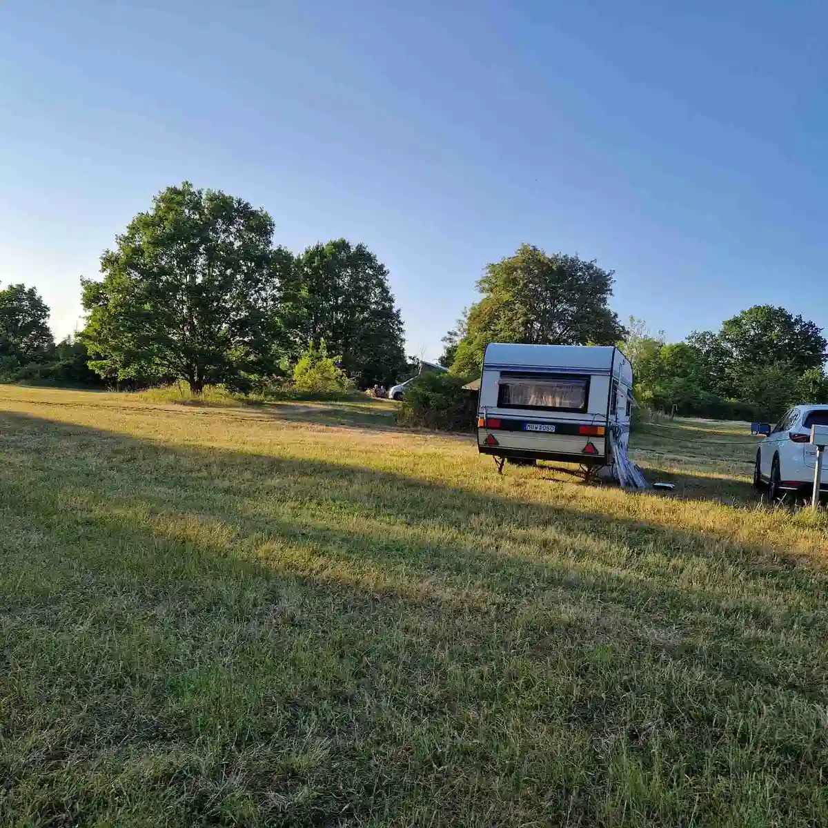 Utsikt över en campingplats vid Vättersmålen med husvagnar och husbilar parkerade på ett grönskande fält. Omkringliggande ängar och gräsytor skapar en lugn och naturskön atmosfär.