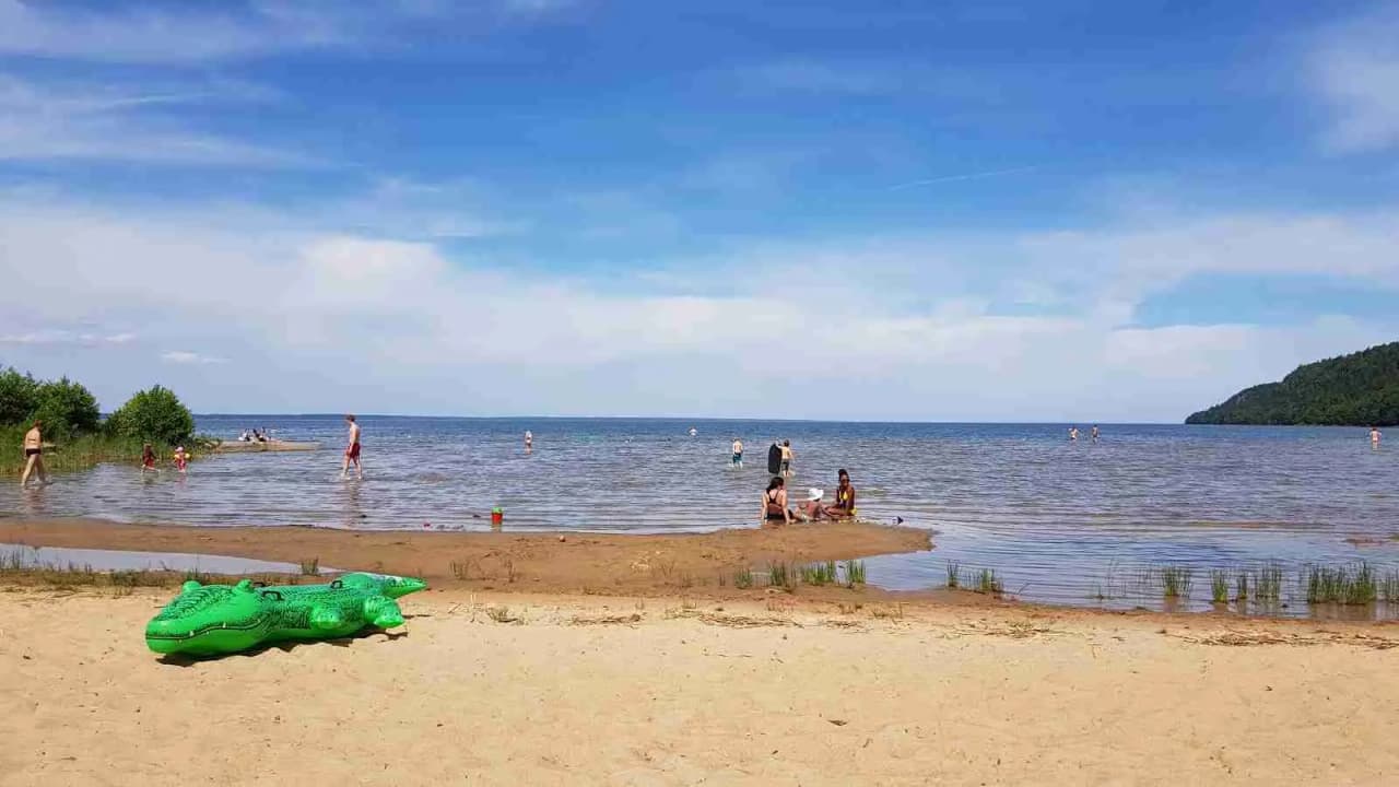 En somrig strand vid Sikhalls camping med människor som njuter av sol och bad vid vattnet.