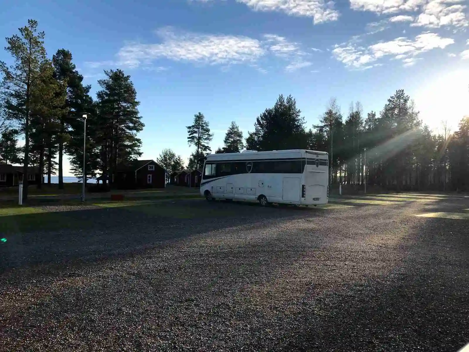 En husvagn och en husbil parkerade nära en campingstuga längs en grusväg på Skellefteå camping, omgivna av grönska och träd.