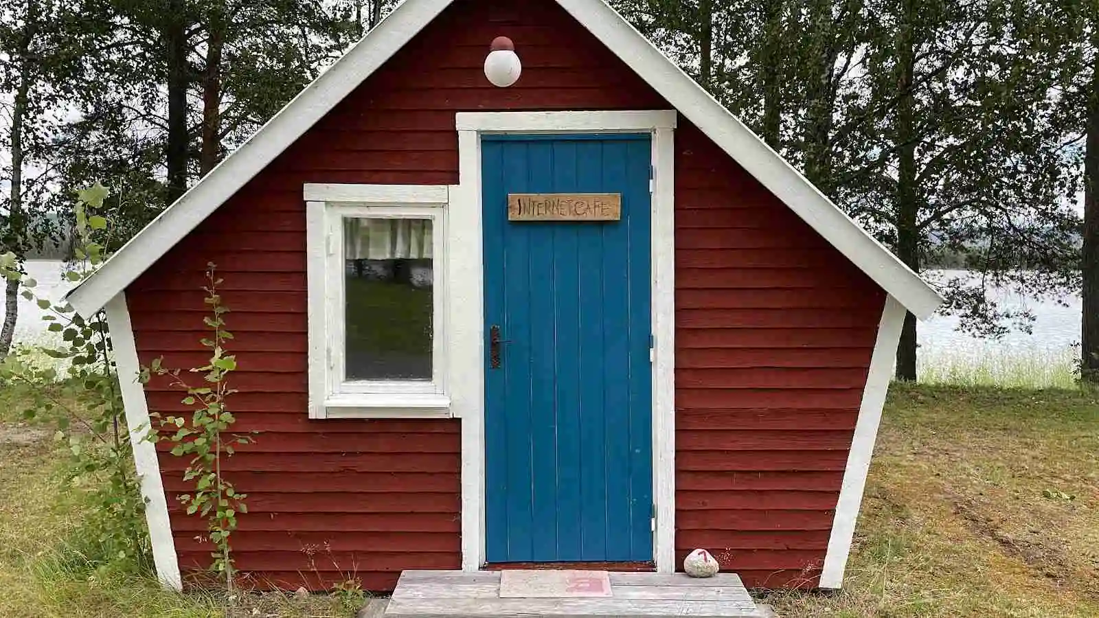 En trästuga med en brun fasad och dörr, omgiven av grönska, vid Trollforsen Camping & Stugor.