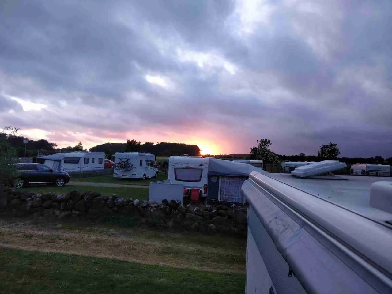 En husbil står parkerad vid Rödlix Hostel & Camping i skymningen, omgiven av kvällshimlens mjuka färgtoner med moln.