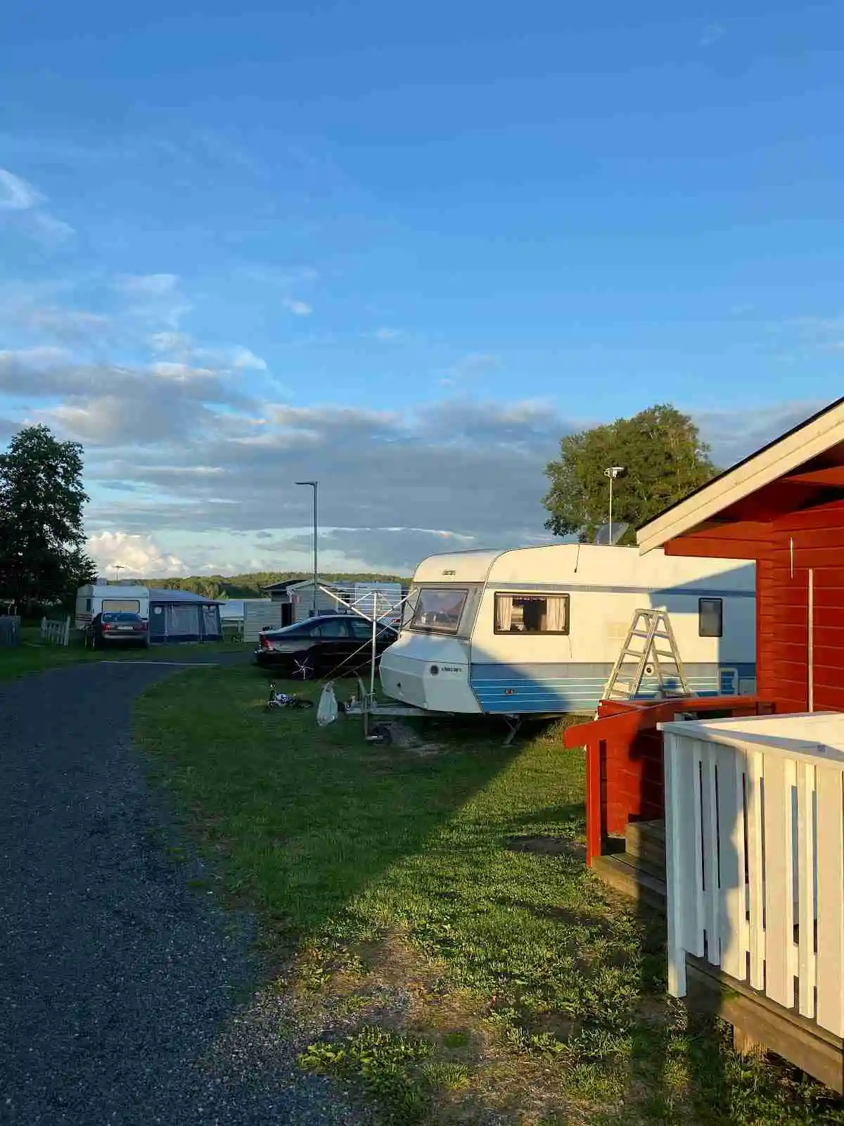 En grön campingplats med husvagnar, tält och parkerade fordon, omgiven av gräsmattor och träd.