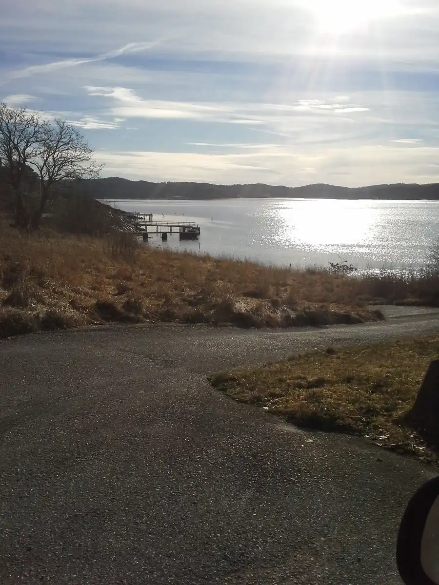 En lugn sjö med molnig himmel i horisonten, omgiven av grönskande kustlinje vid Löfgrens camping.