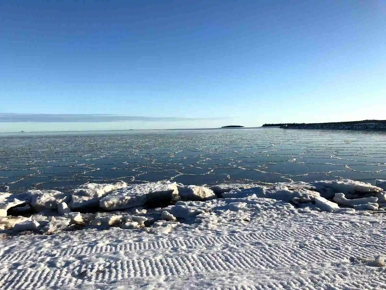 En vintermorgon vid Skellefteå camping med blå himmel, horisont och solens ljus som speglas över det frusna havet.