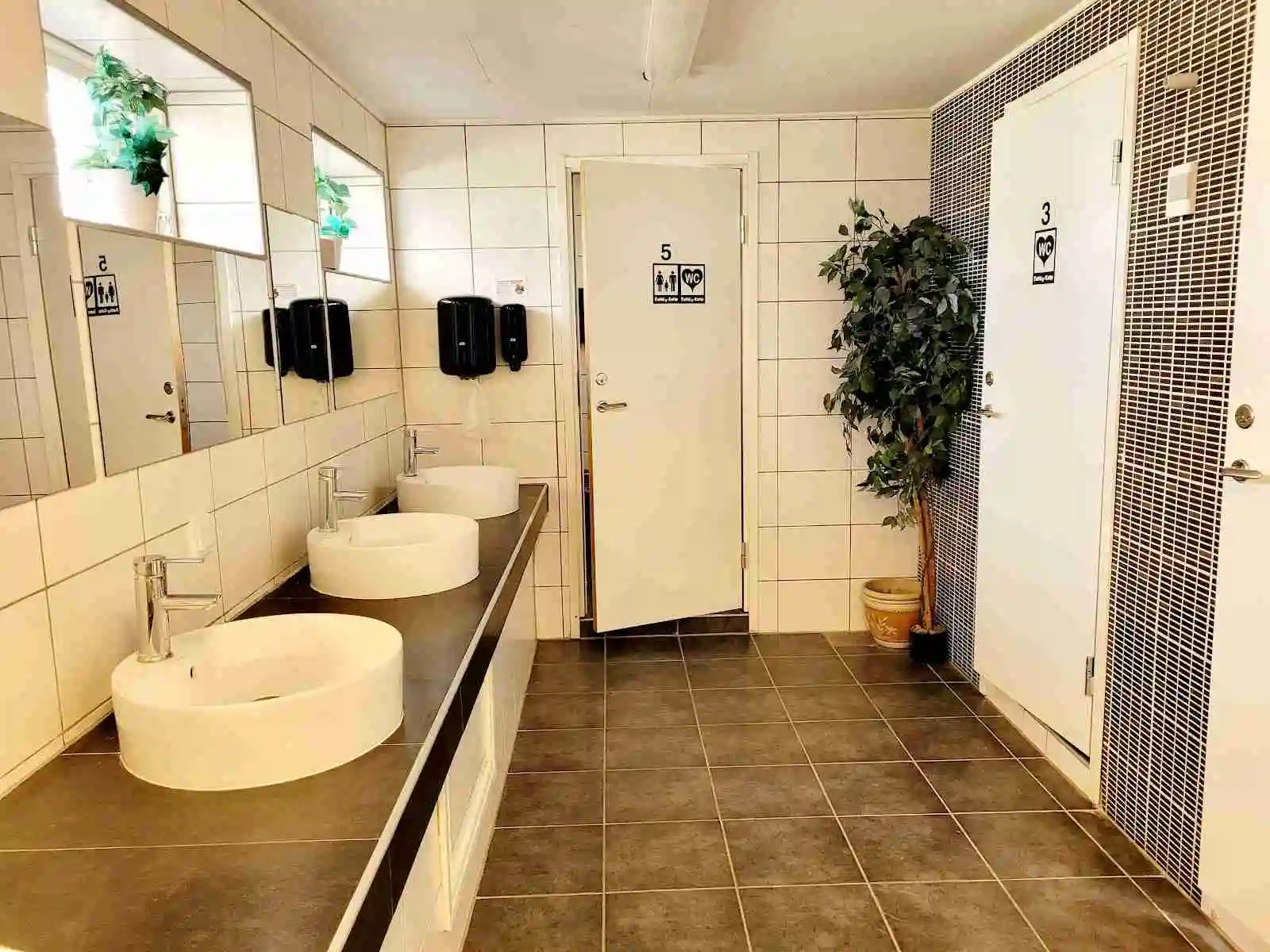 Badrum med vit handfat och spegel, kaklade väggar, och klinkergolv på Charlottenberg camping & stugor - Haganäset.