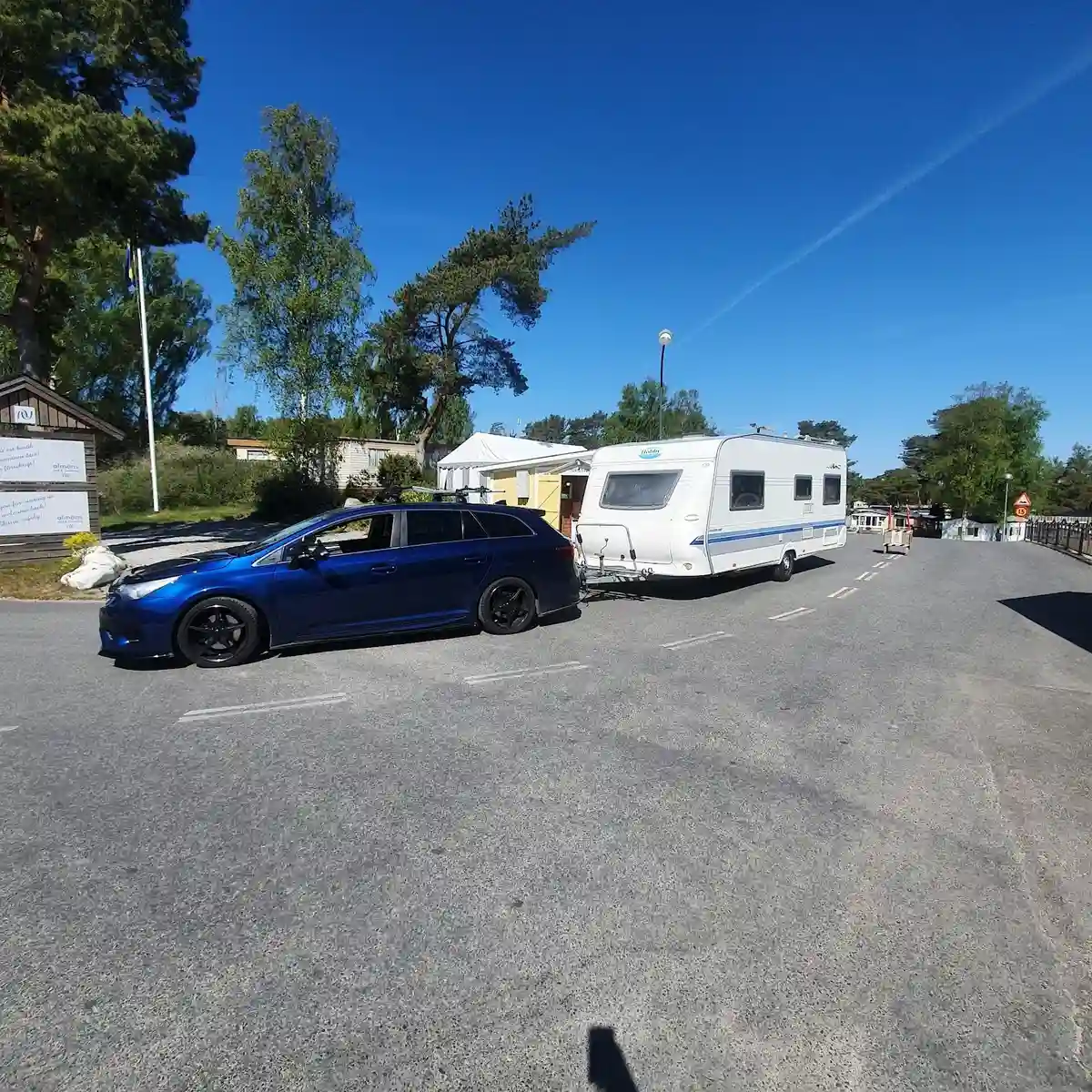 En parkeringsplats med flera bilar uppställda vid Almöns Bad & Camping, omgiven av grönska och träd i bakgrunden.