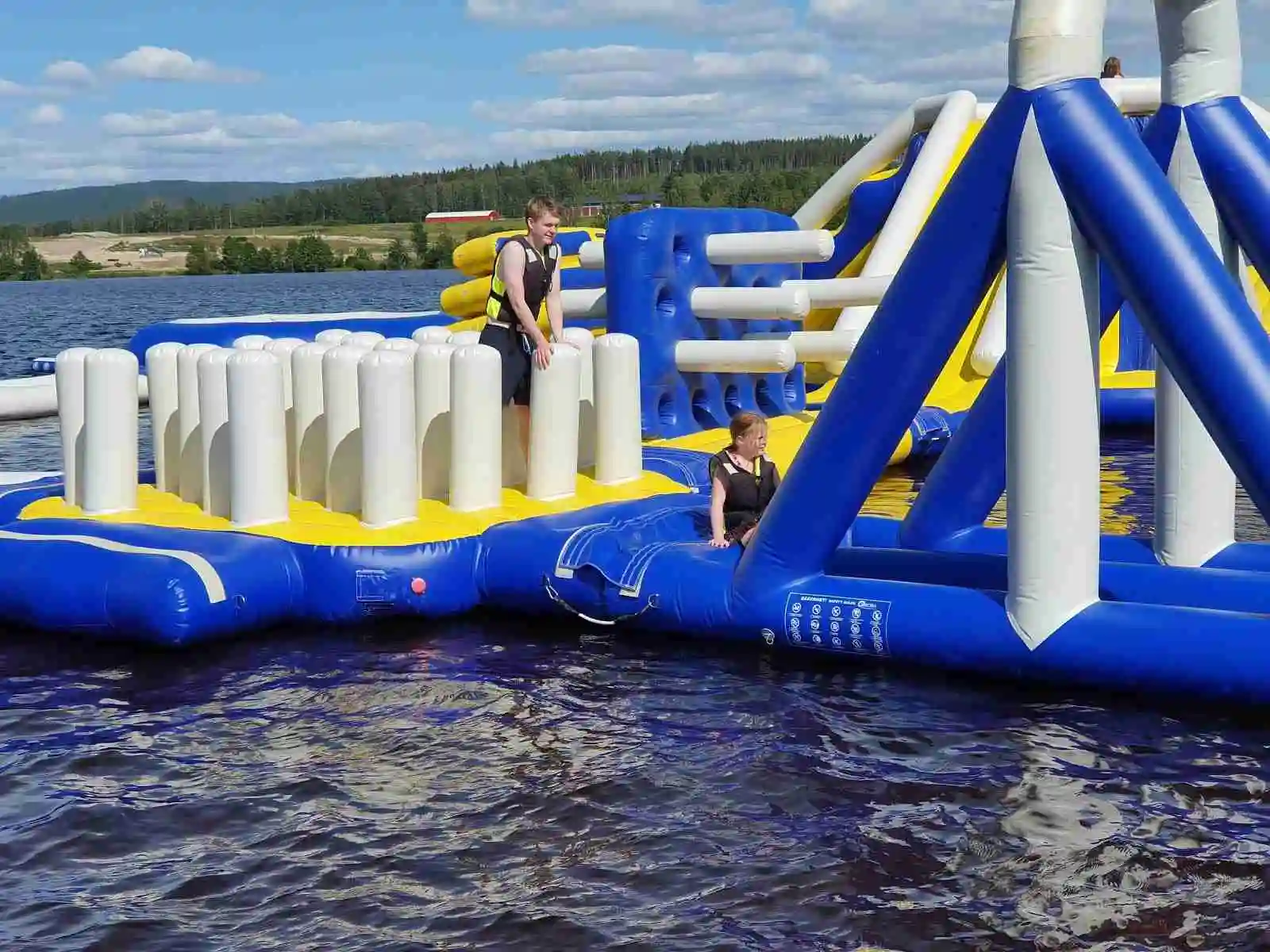 En färgglad uppblåsbar vattenlekplats med glada människor som åker på vattenrutschbanor och leker på flotten i en stor swimmingpool, omgivna av somrig natur vid Sunne Camping och Sommarland.