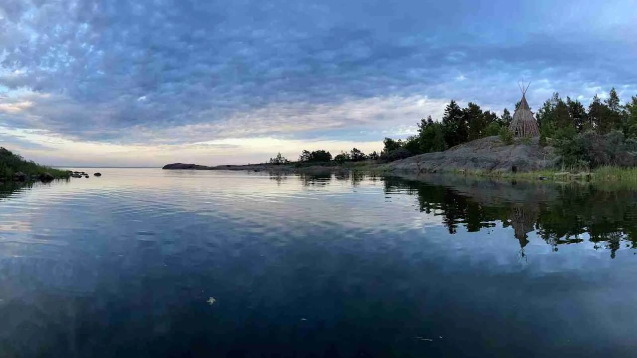 Vy över havet med moln på himlen, en vattenväg leder in mot en kustlinje kantad av träd.