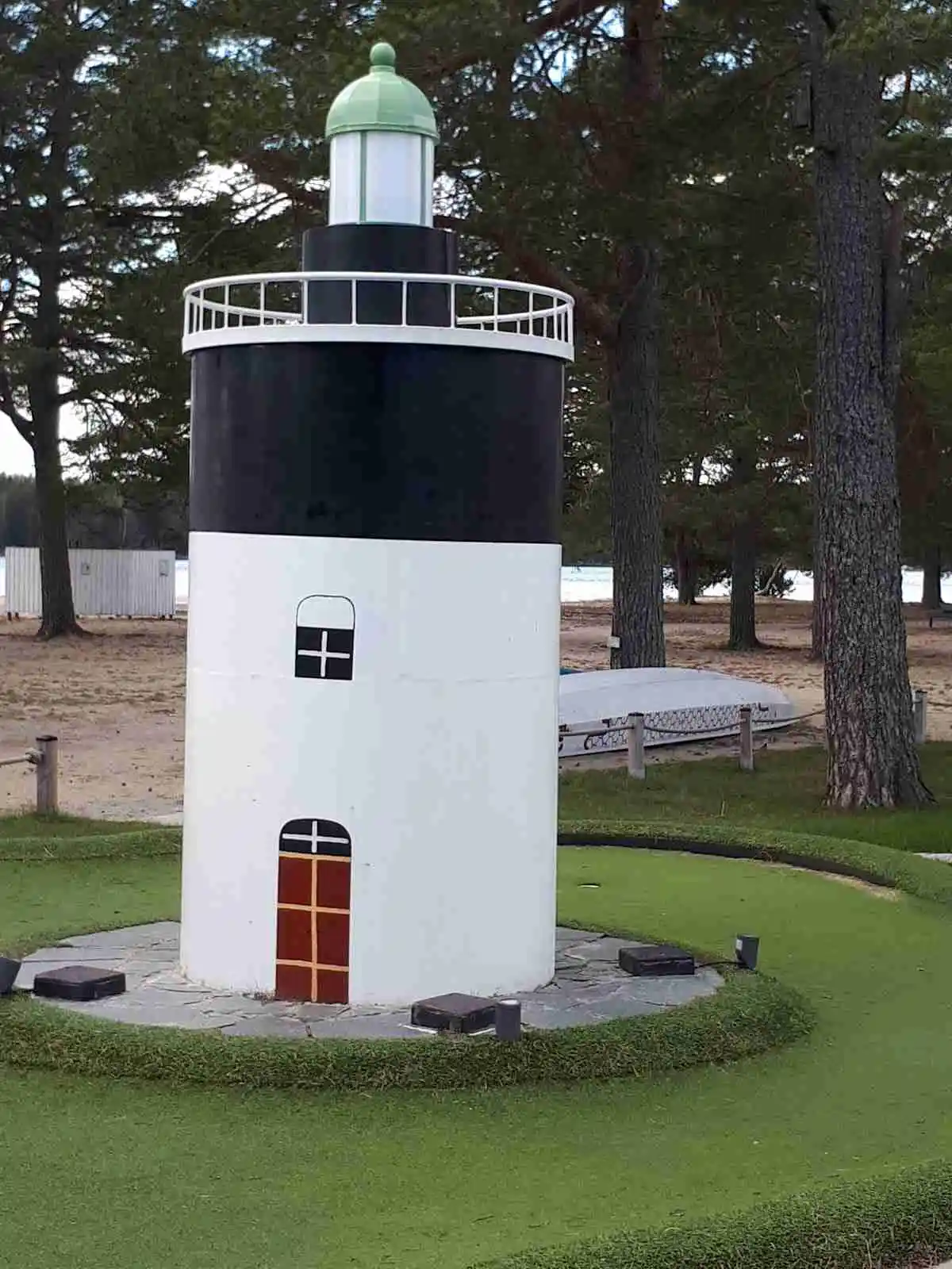 En fyr i cylinderform står omgiven av grönskande gräsmattor och en vackert anlagd park, belägen vid Stenö Havsbad & Camping.