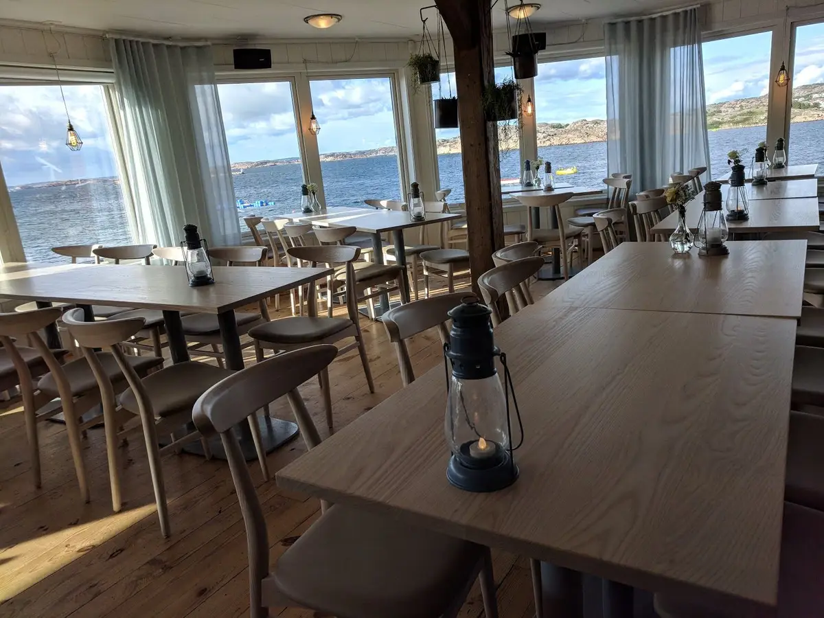 Alt-text: Uteservering med möblerade bord och stolar vid Ramsvik Stugby & Camping, omgiven av naturskön miljö.