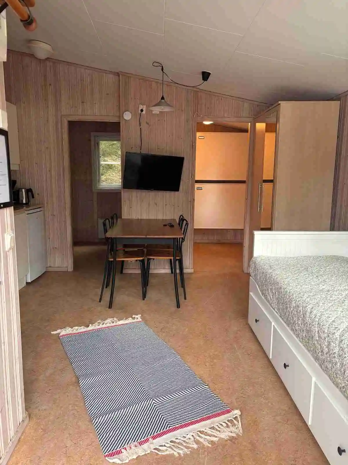 En inbjudande campingstuga med träinredning, möbler och en bekväm säng i ett sovrum där golv och tak harmonierar med rummets naturliga och rustika stil.