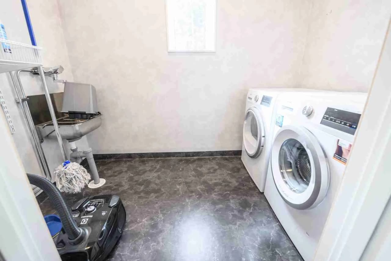 En modern tvättstuga på Östersunds camping med tvättmaskin, torktumlare och silverfärgade detaljer. Rummet har kaklat golv och väggar samt en praktisk inredning.