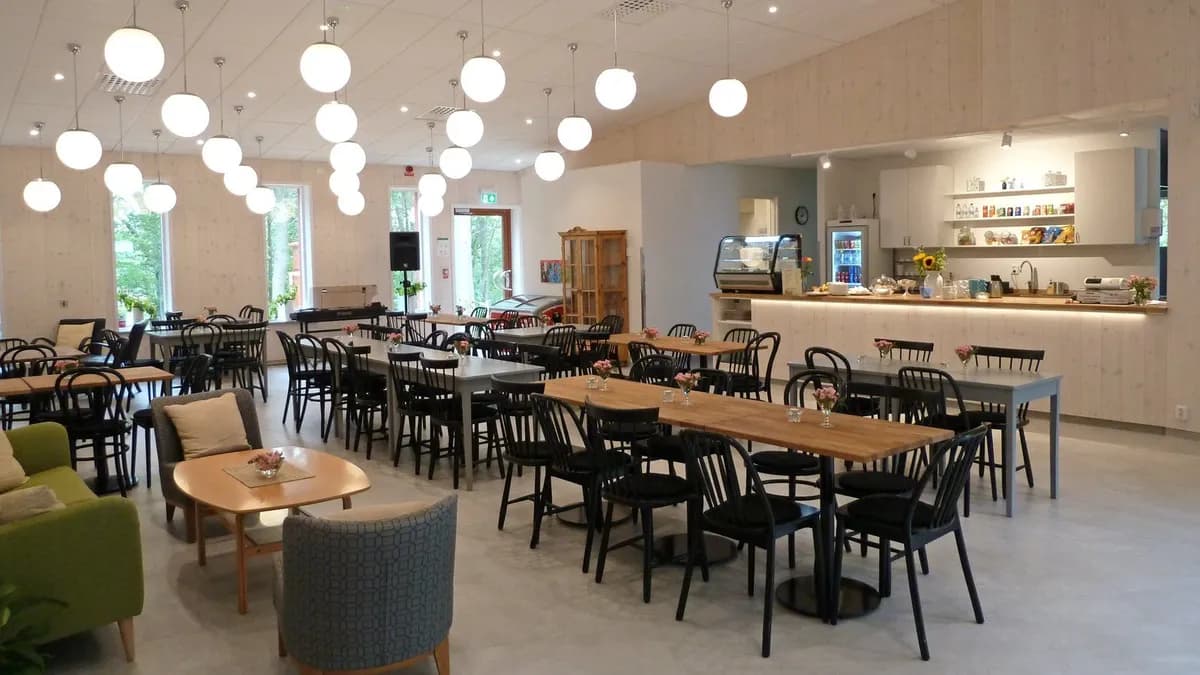 En rymlig och ljus restauranginteriör med flera bord och stolar, inrett med trädetaljer och stora fönster.